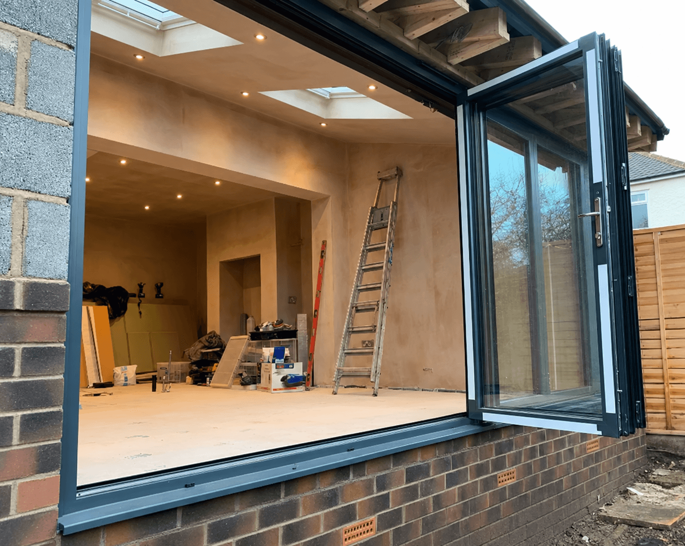 Waterfield extension during construction with exposed roof timbers, newly plastered walls, rooflights and fitted bifold doors